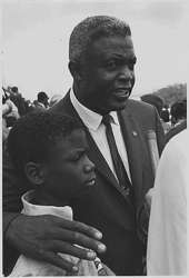 black man with his arm around a black boy speaks into a microphone 